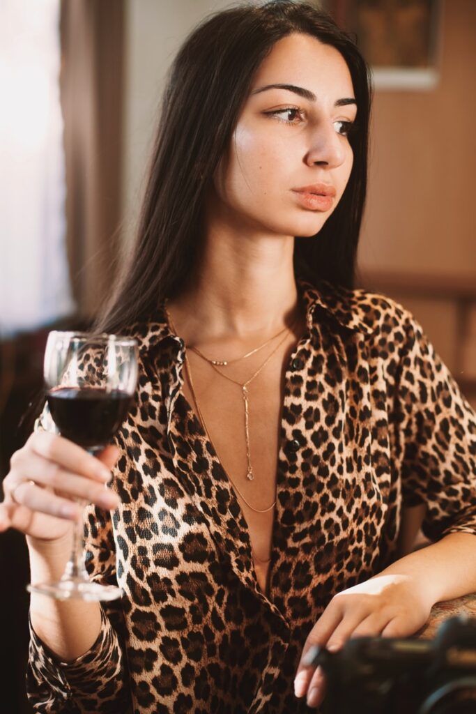 woman in brown and black leopard print long sleeve shirt holding clear wine glass
